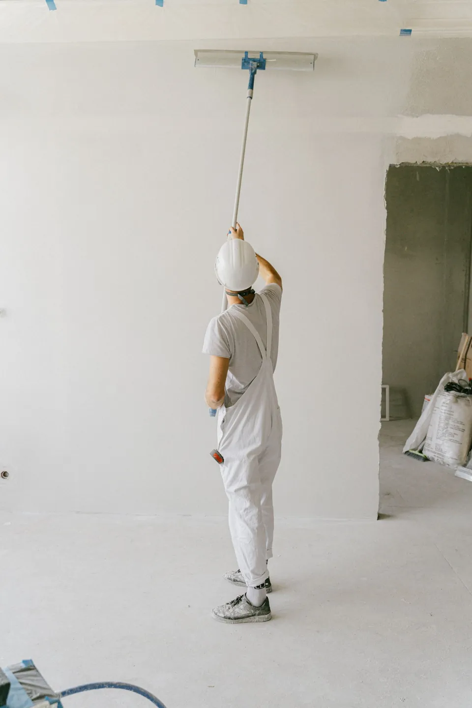 Painter in whites rolling a ceiling with an extension pole in an empty room